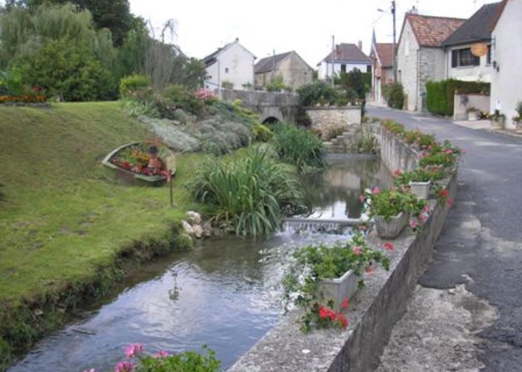 Une petite rivière traverse un petit village entouré de maisons et de fleurs.